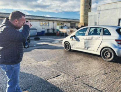 Das Bild zeigt einen Mitarbeiter vom Kfz Sachverständigenbüro Natzius in Grimmen beim Fotografieren eines Fahrzeugschadens zur Erstellung von einem Kfz Unfallgutachten.
