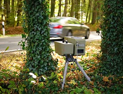 Das Bild zeigt eine mobile Radarfalle, die im Wald steht. Ein Auto fährt zu schnell vorbei und wird geblitzt. Kfz Sachverständige in Teterow von der Firma Natzius prüfen Ordnungswidrigkeiten, wenn du gegen Rotlichtverstöße oder Geschwindigkeitsüberschreitungen vorgehen möchtest.
