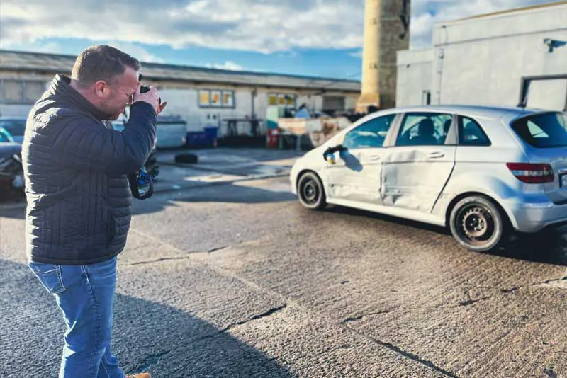 Das Bild zeigt einen Unfallgutachter in Teterow von Kfz-Natzius dabei, wie er einen Schaden an der linken Seite eines Autos fotografiert.