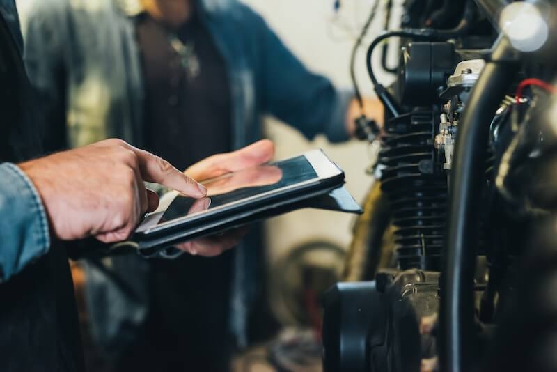 Das Bild zeigt zwei Personen neben einem Motorrad. Eine Person hält ein Tablet und symbolisiert damit die Erstellung von einem Motorradgutachten in Neustrelitz zur Aufnahme eines Haftpflichtgutachtens von Natzius.